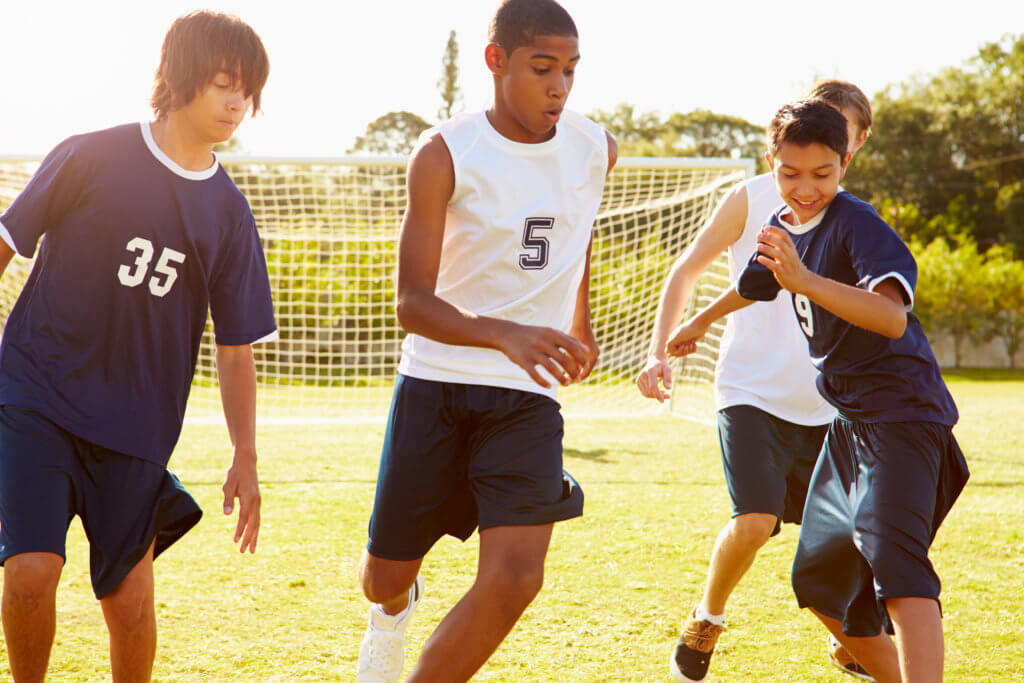 Group of multiracial male teens play soccer on a field.