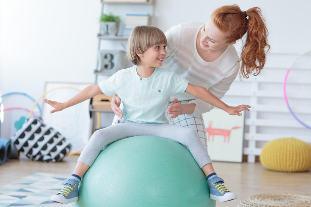 Young boy balances on an exercise ball during a physical therapy session. 