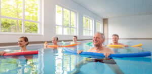 Group of older adults in swimming pool with foam flotation devices doing aquatic aerobics