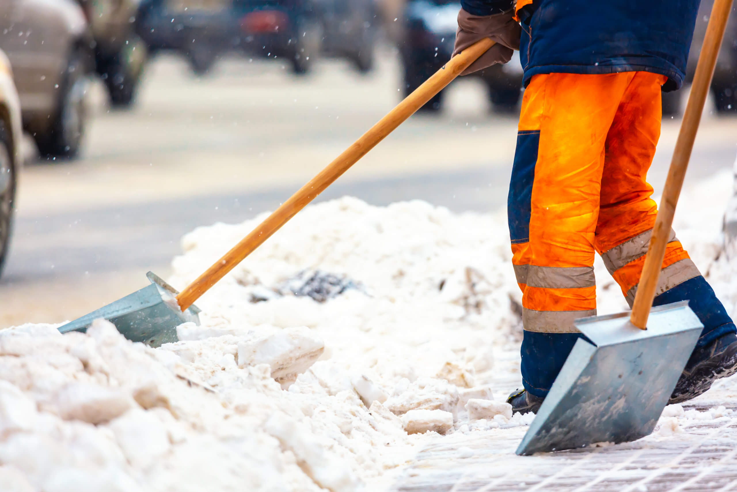 Man in orange work pants shovels a sidewalk to remove the snow. 