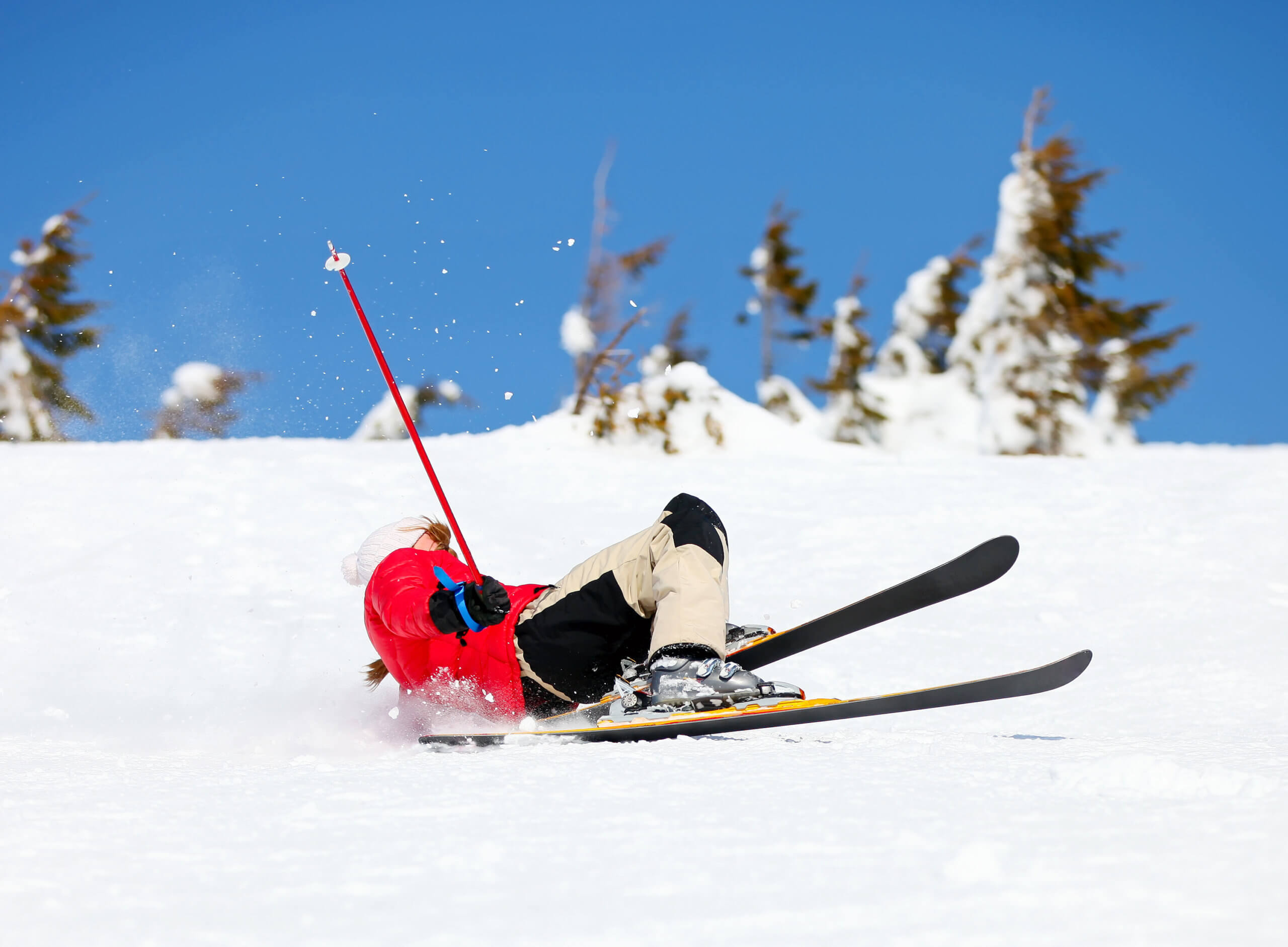 Skier in red jacket falls as he descends a ski slope.
