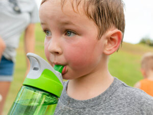 A young boy with a red face sweats while drinking from a water bottle.