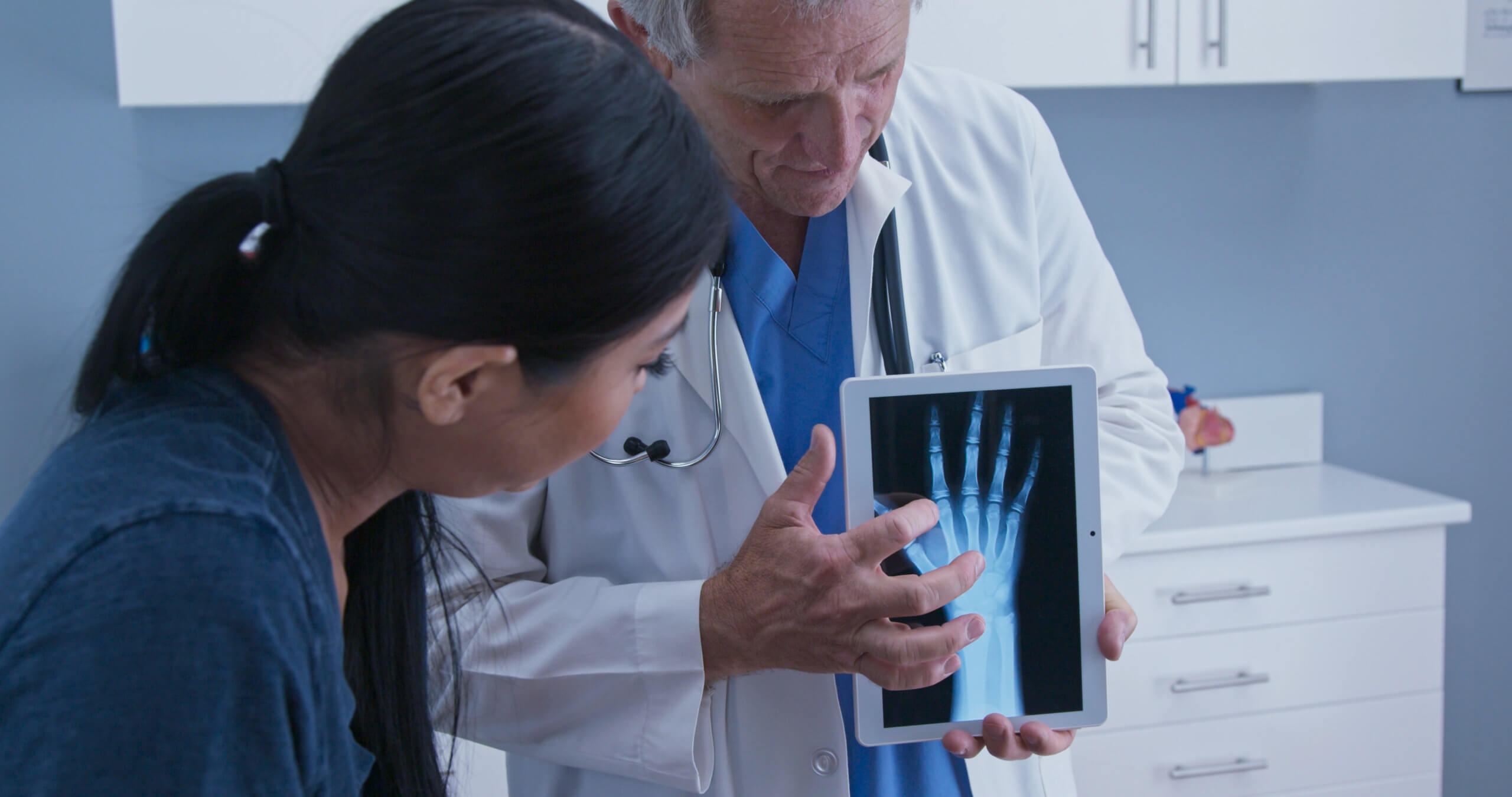 A male doctor shows a female patient an X-ray of her hand.