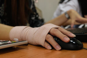 A woman uses her computer mouse while wearing a wrist bandage.