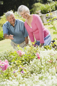 Happy older couple enjoys looking at flowers in bloom in the local botanical garden.