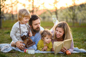 Family with two young children and camera or binoculars look at a book outdoors in the spring.