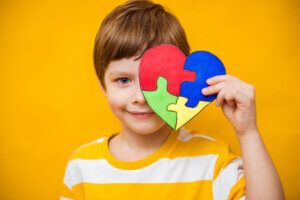 A boy holds a heart-shaped puzzle, a symbol of autism awareness, in front of his face.