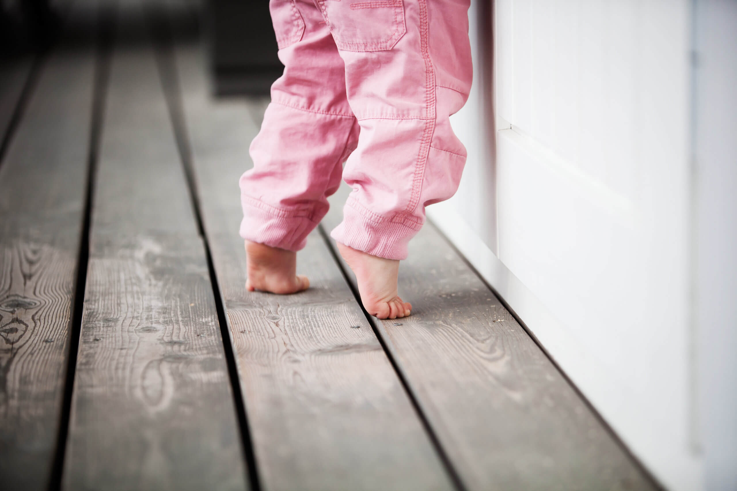 A little girl in pink pants stands on her toes. 