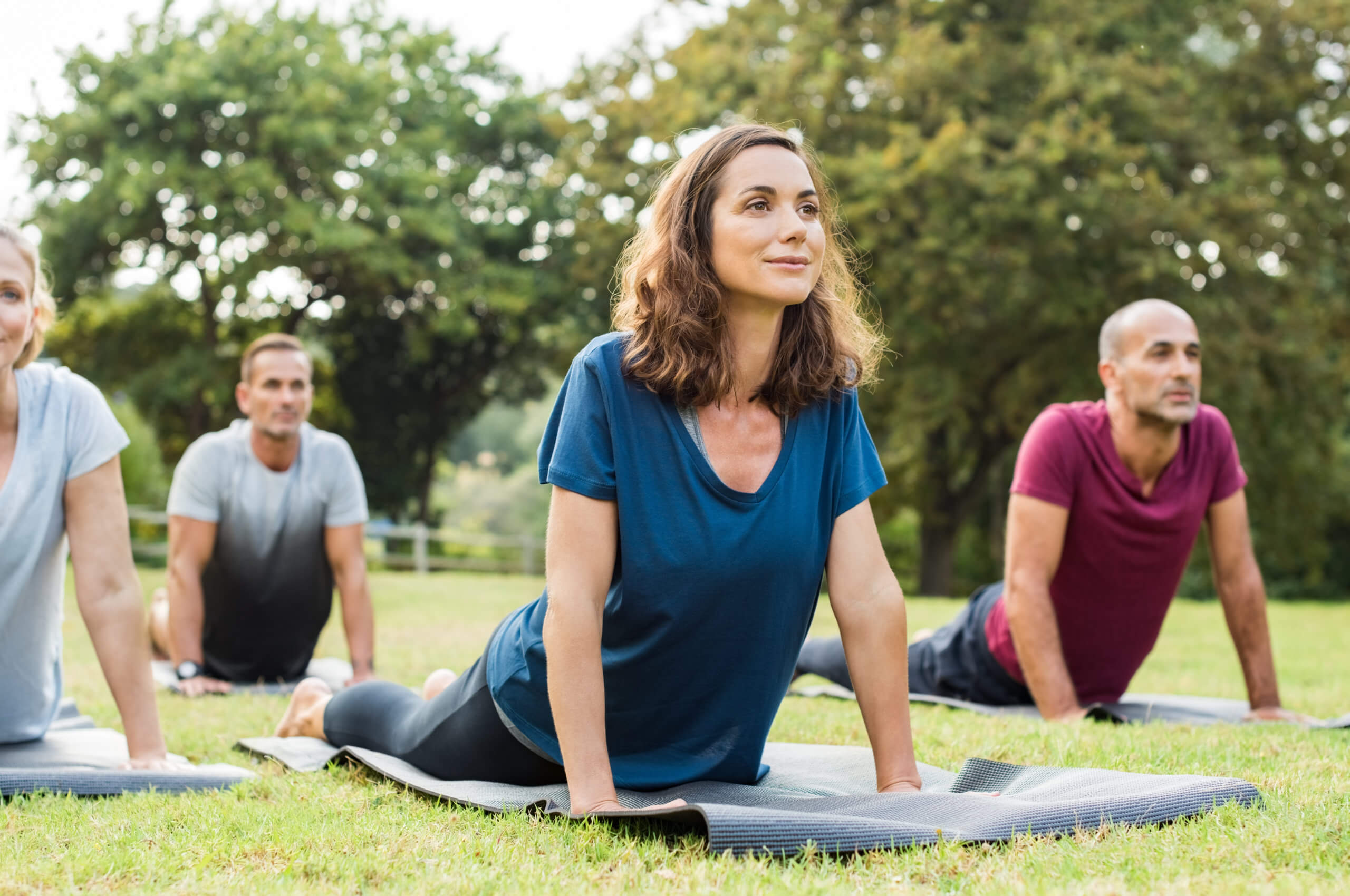  A group of men and women hold a pose while practicing yoga in a park.