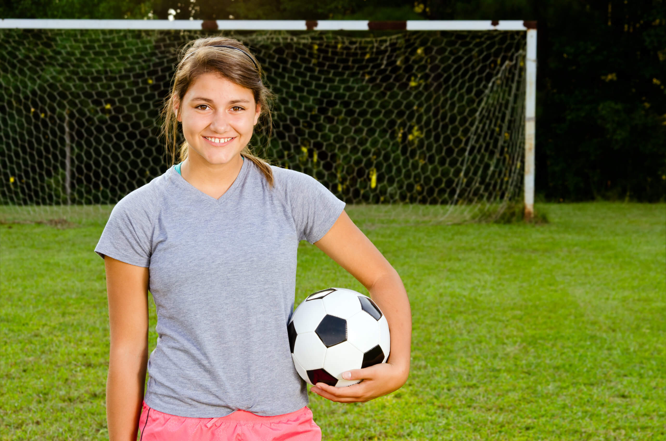  Young teen girl holds a soccer ball on the field in front of a goal. 