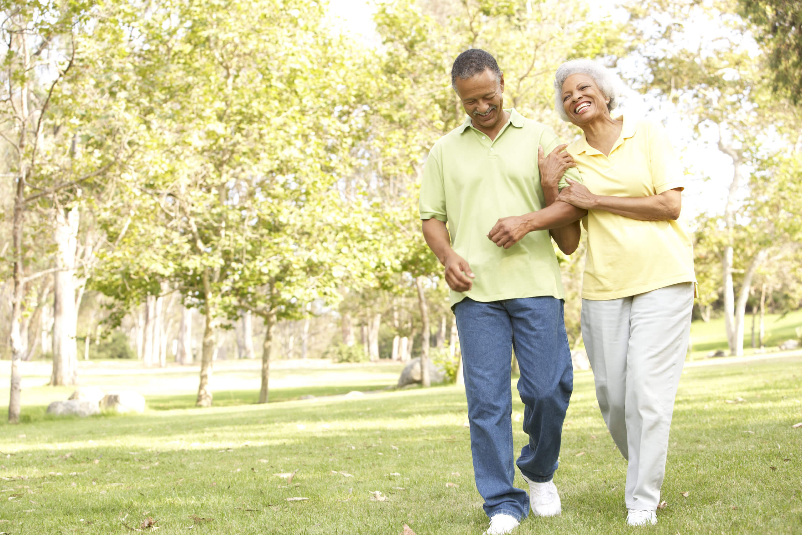 Smiling older Black couple walks together in a park in Long Island, NY.