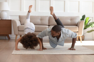 A Black father and daughter do yoga together in their home to help reduce the symptoms of juvenile arthritis.