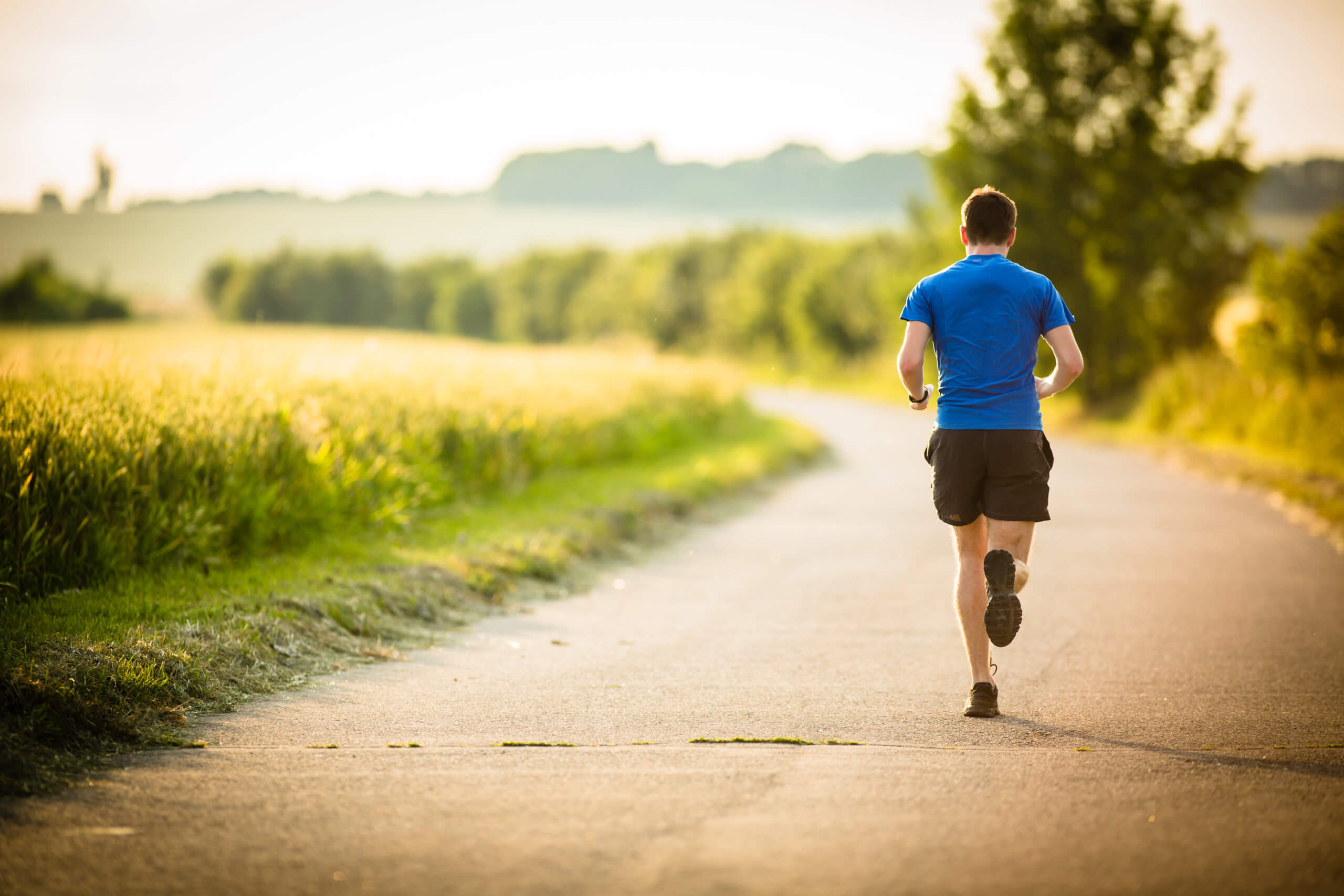 Male jogger runs along a country road early in the morning. 