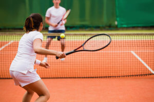 A female in tennis whites prepares to hit the ball back to her male opponent on the tennis court.