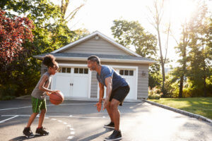 Father and daughter play basketball in the driveway of their suburban home.