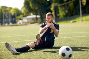 Young male athlete holds his knee in pain after being injured on a Long Island soccer field.