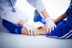 Pediatric orthopedic specialist wearing gloves assesses bruised area of child’s sport-related knee injury.