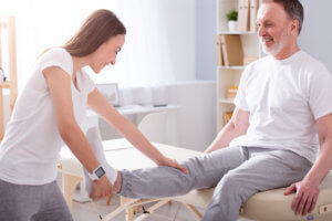 A female physical therapist works with a male patient recovering from a knee injury.