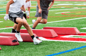Young football players wearing football cleats with ankle support practice on the field.