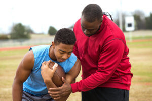 A football coach shows a young player how to carry the ball and avoid injury.