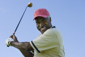Older man smiles while swinging a golf club.