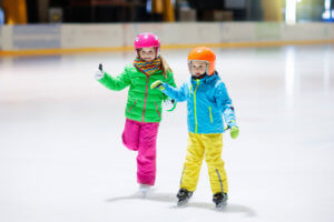 Children wearing helmets learn to skate on a rink.