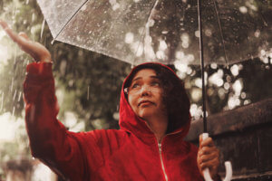 Woman in red coat walks in a park with an umbrella during a rainstorm.