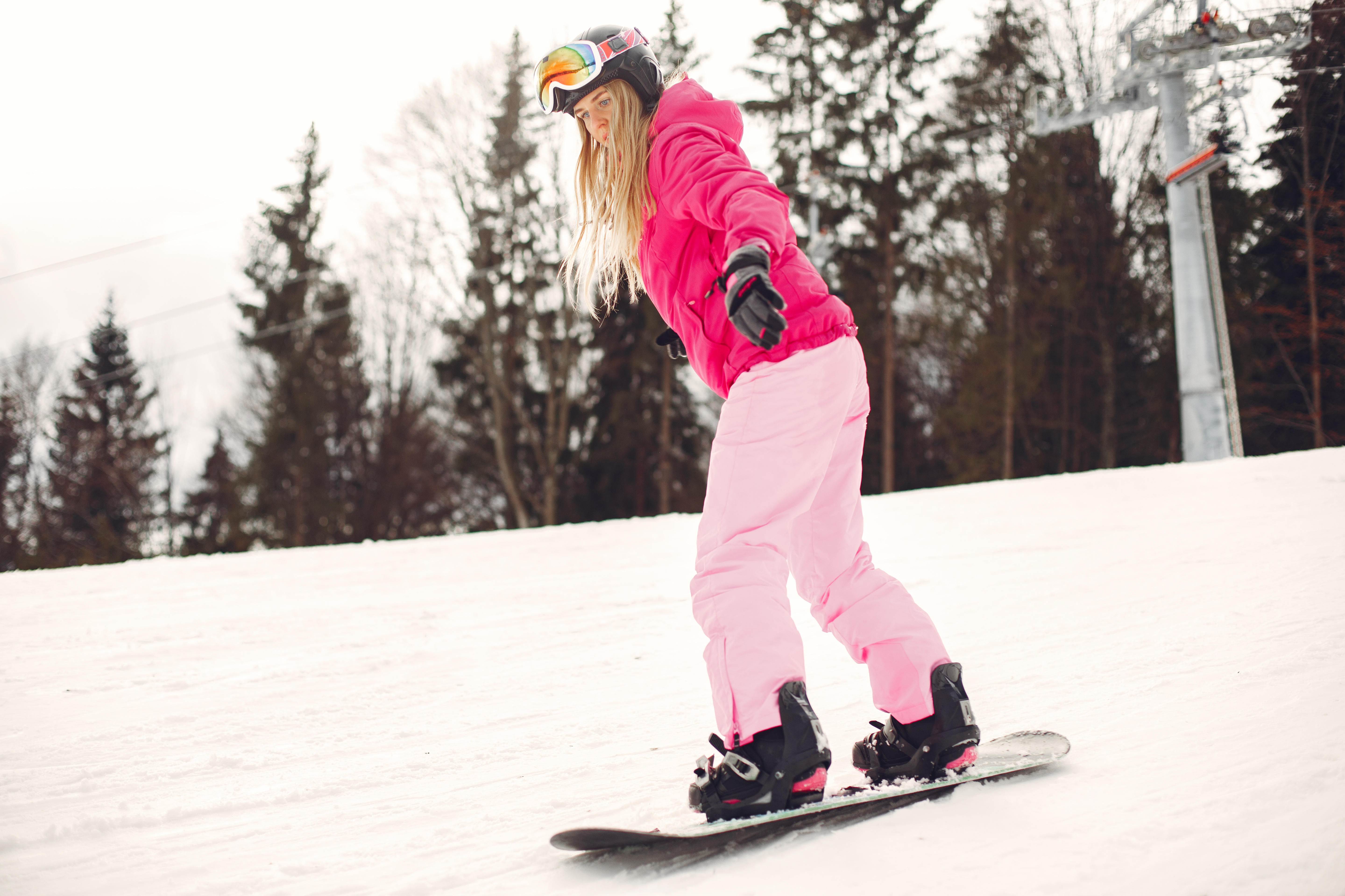  Teenage girl in pink coat and pants snowboards on a hill. 