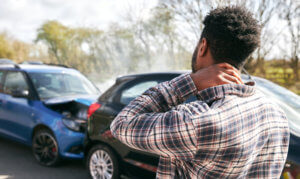 Man stands in front of a car accident with his neck in pain.