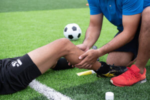 Soccer player on the ground as a medical professional inspects their knee.