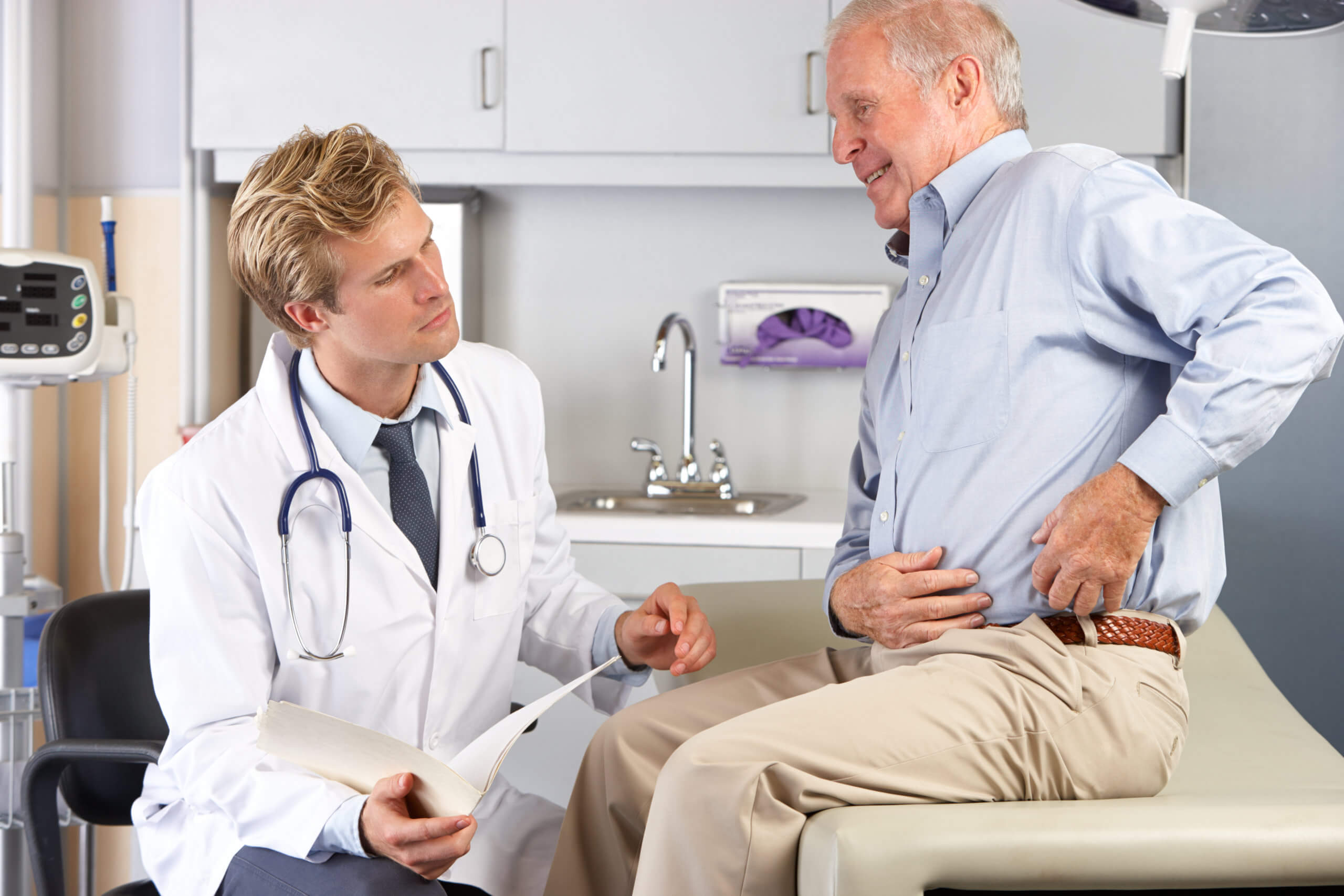An elderly man shows a doctor where his hip pain is located.