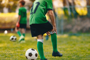 A young boy stands on a soccer field in uniform and holds his knee.