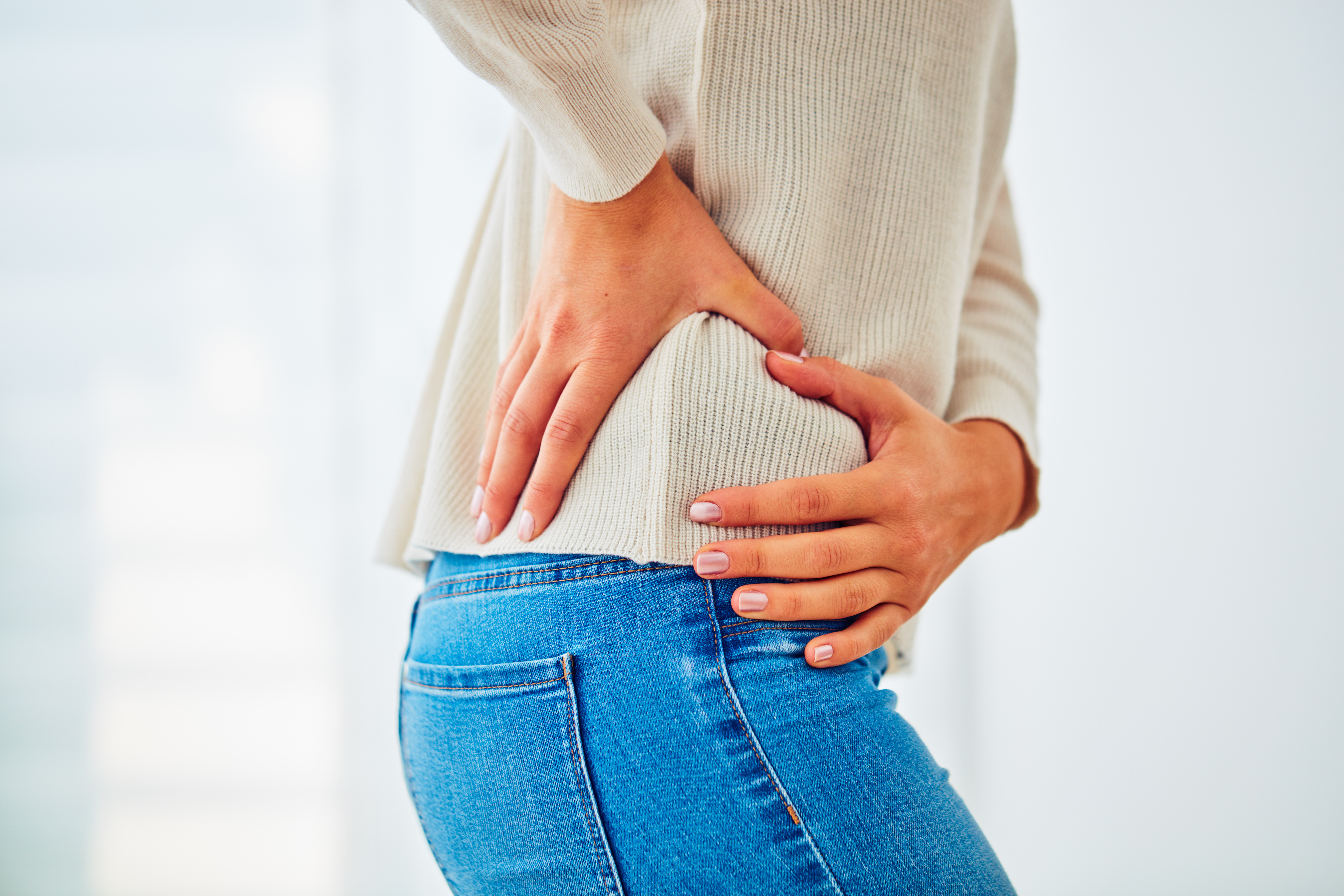 Woman in jeans holds her hip and lower back in pain. 