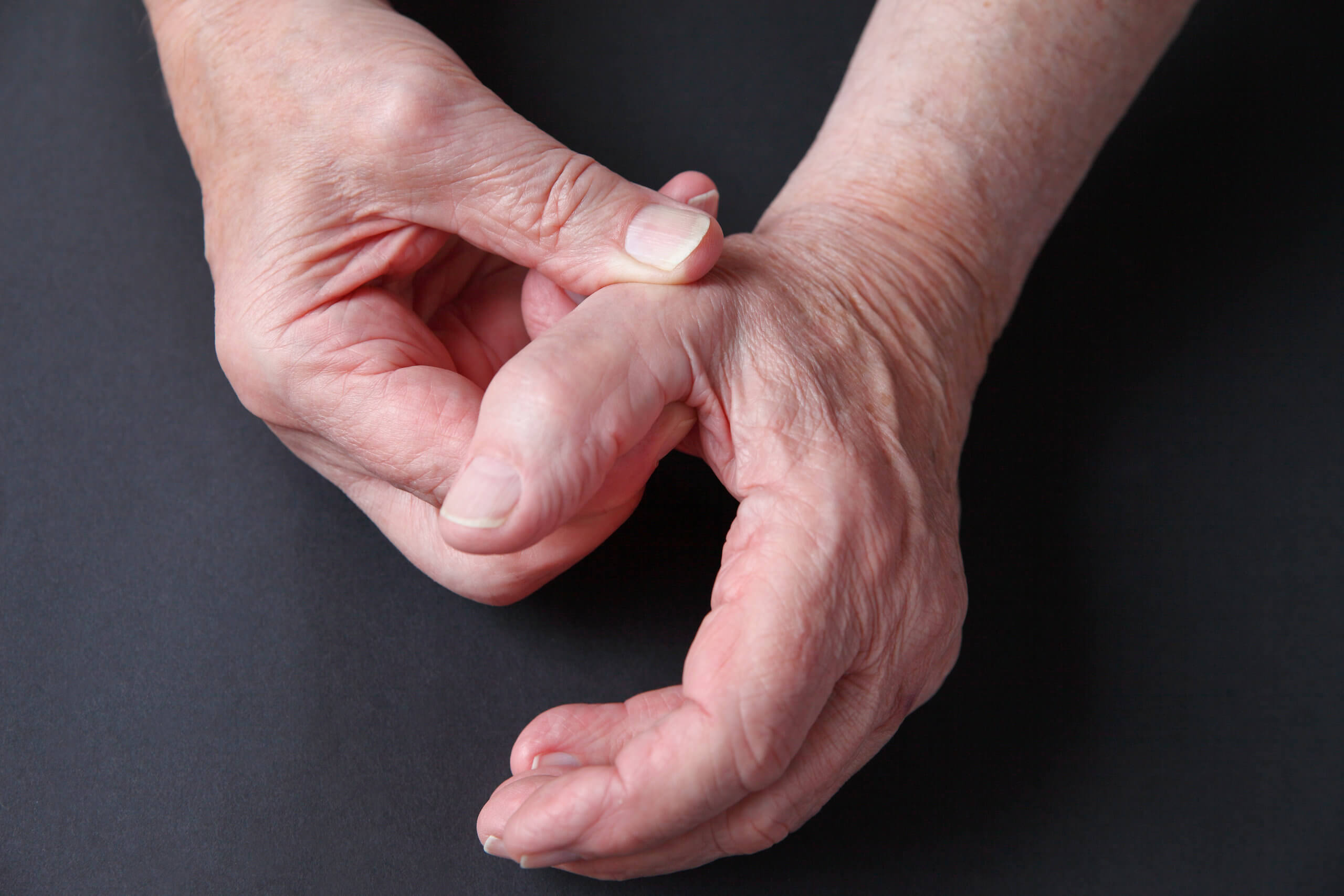 An older man rubs the base of his thumb with the other hand. 