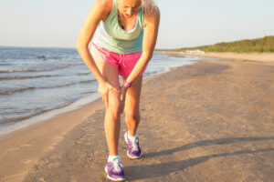 A woman running on the beach stops and holds her knee in pain.