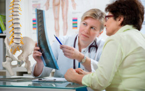 An orthopedist holds up a spinal X-ray and explains the results to her patient.