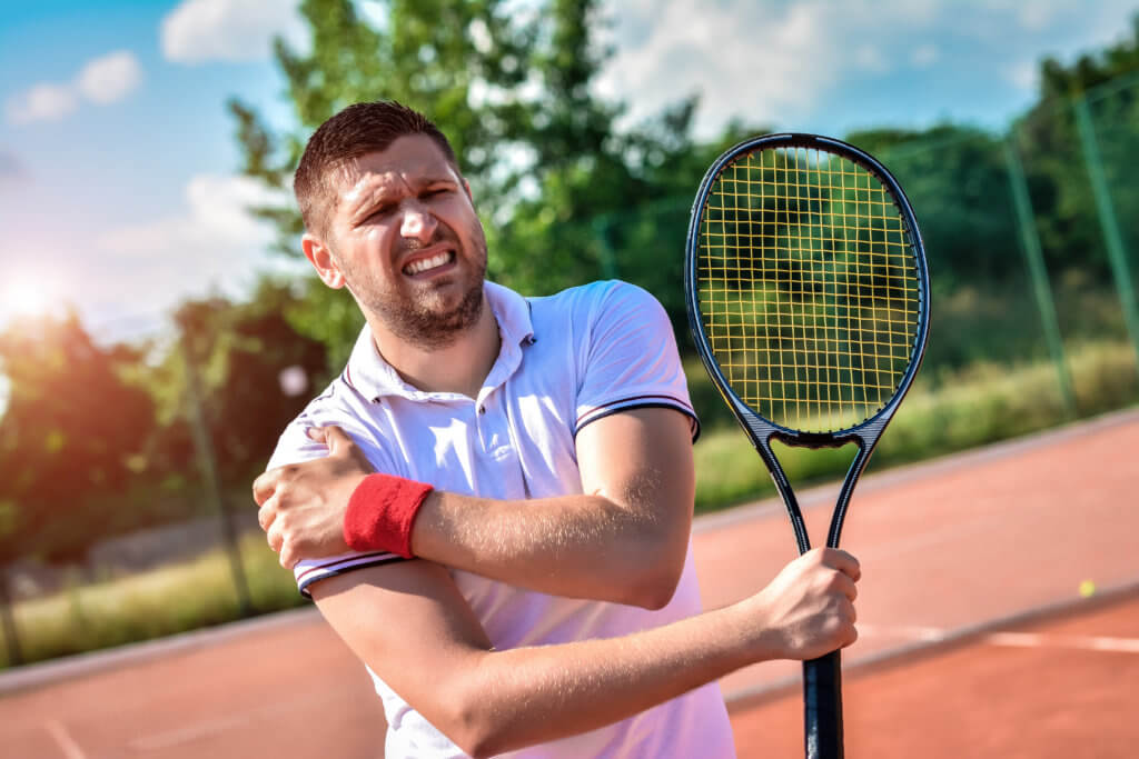  A young man on a tennis court holds a racket in one hand and holds his shoulder in pain with the other. 
