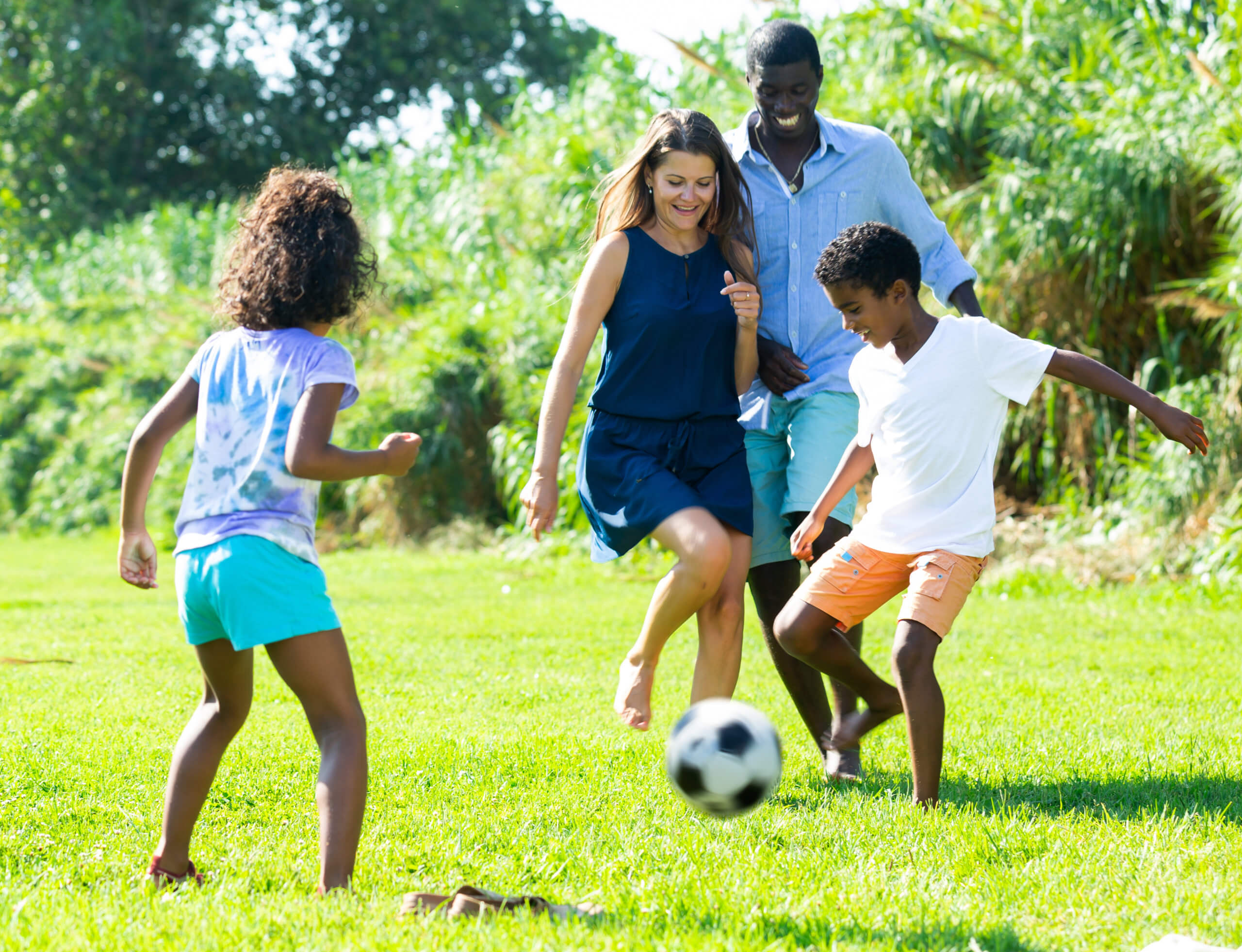 A young family of two parents and two children kick around a soccer ball outside.