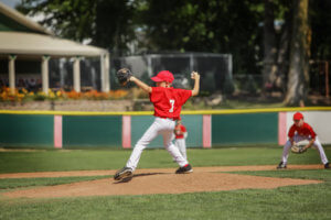 Young baseball pitcher in red jersey is throwing the ball to the batter.