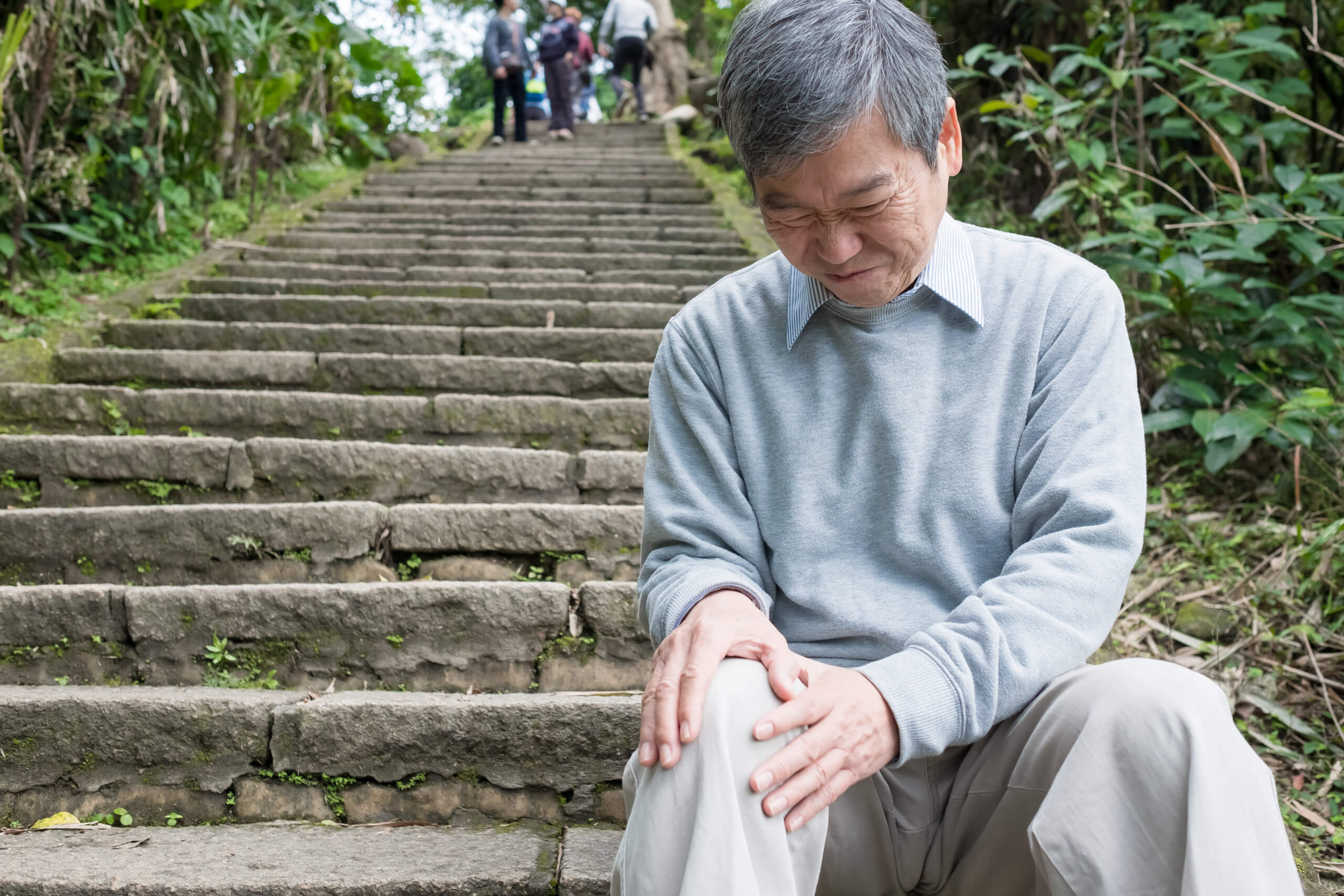 A senior man sits on the steps as his painful knee prevents him from continuing.