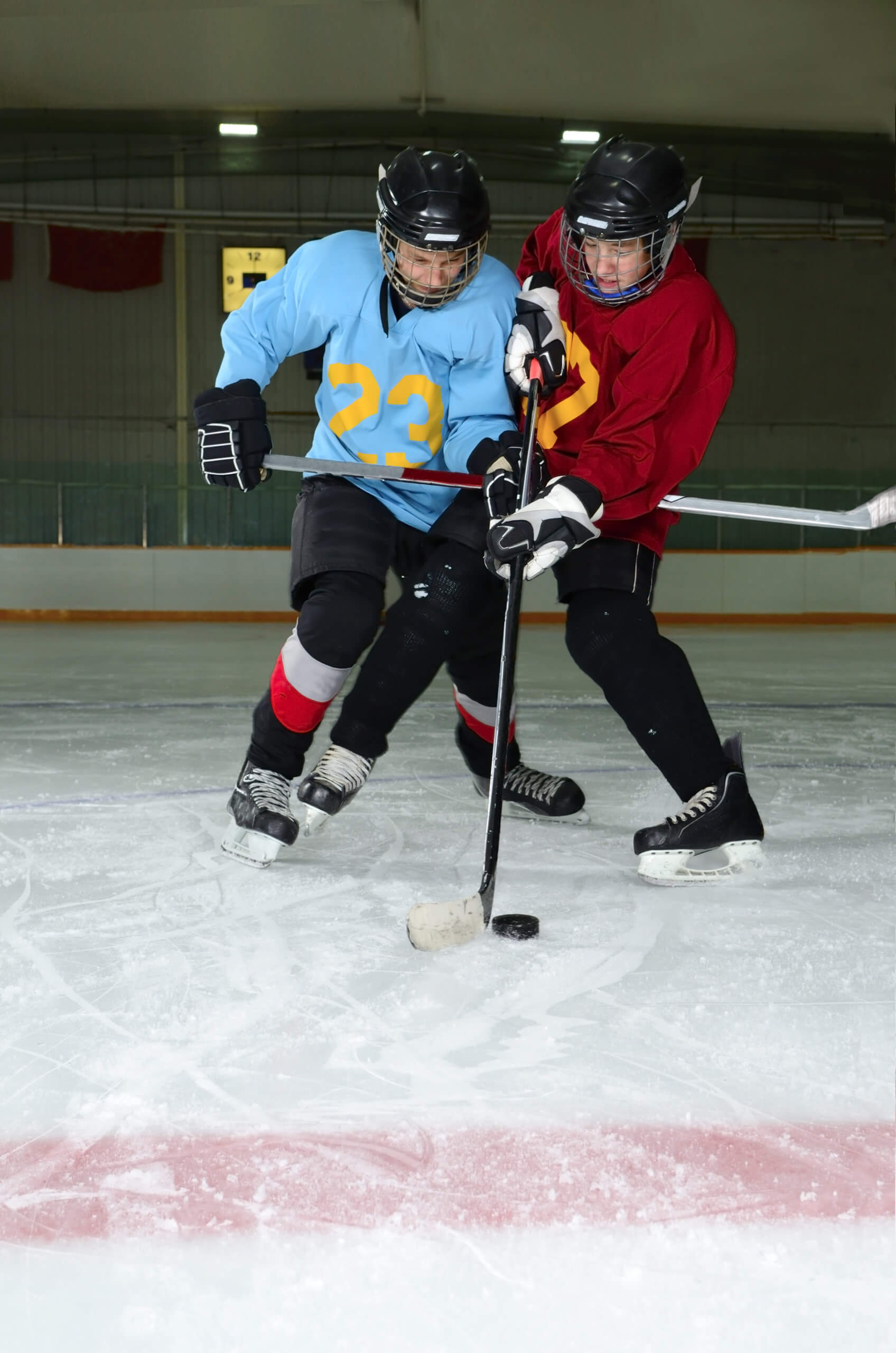 Two teen boys collide shoulder-to-shoulder while playing hockey on an indoor rink. 