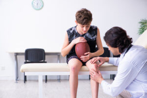 Young football player sits in doctors office as the doctor inspects his knee.