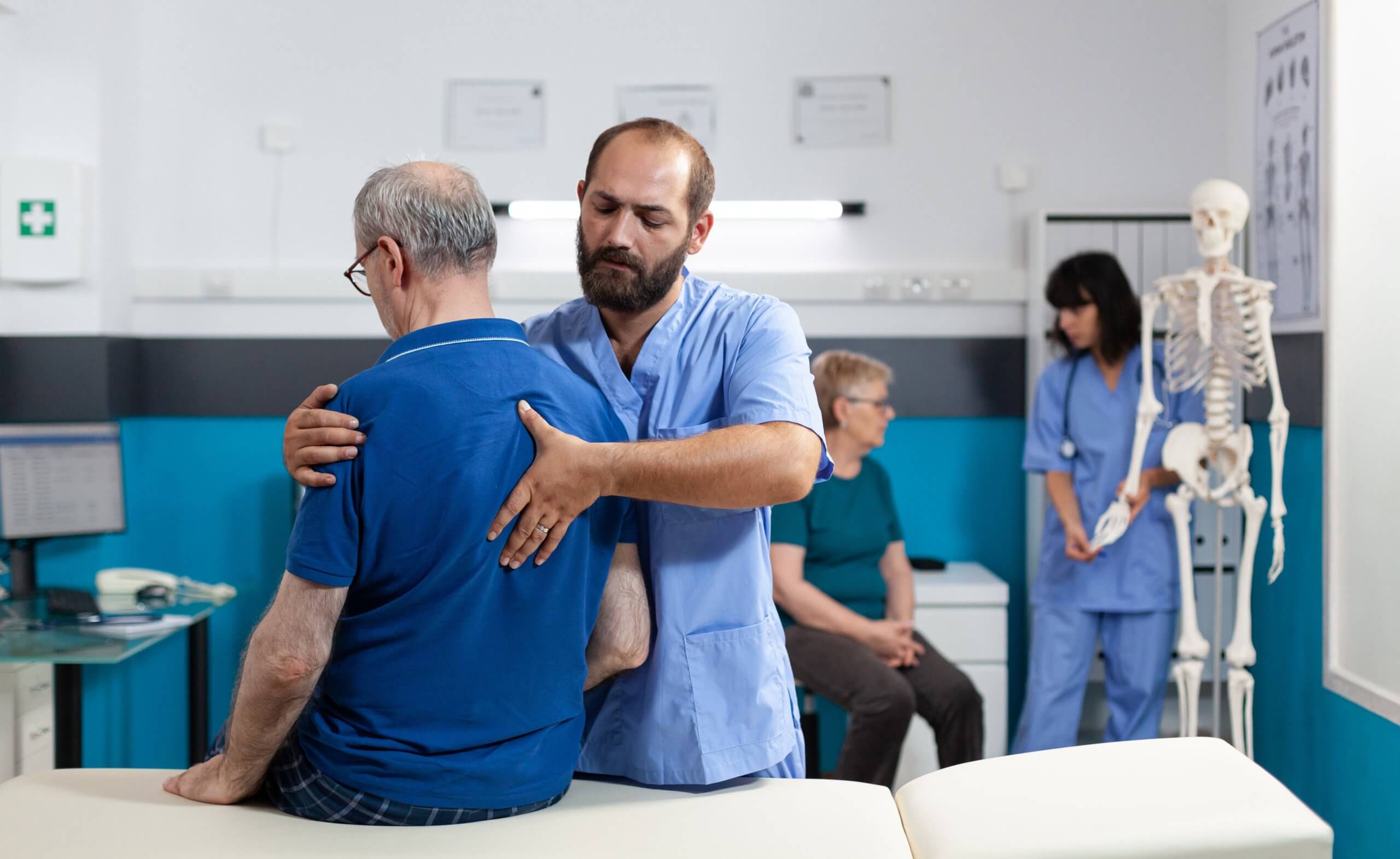  A male medical professional examines an older man’s back as he sits on a table. 