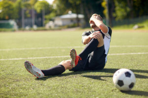 Soccer player lays on the ground and clutches his knee in pain after taking a fall.