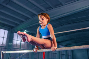 A young girl holds a gymnastics pose on the uneven bars.