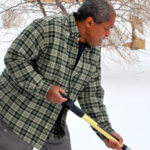 Black man in a plaid shirt clears his driveway after a snowstorm.