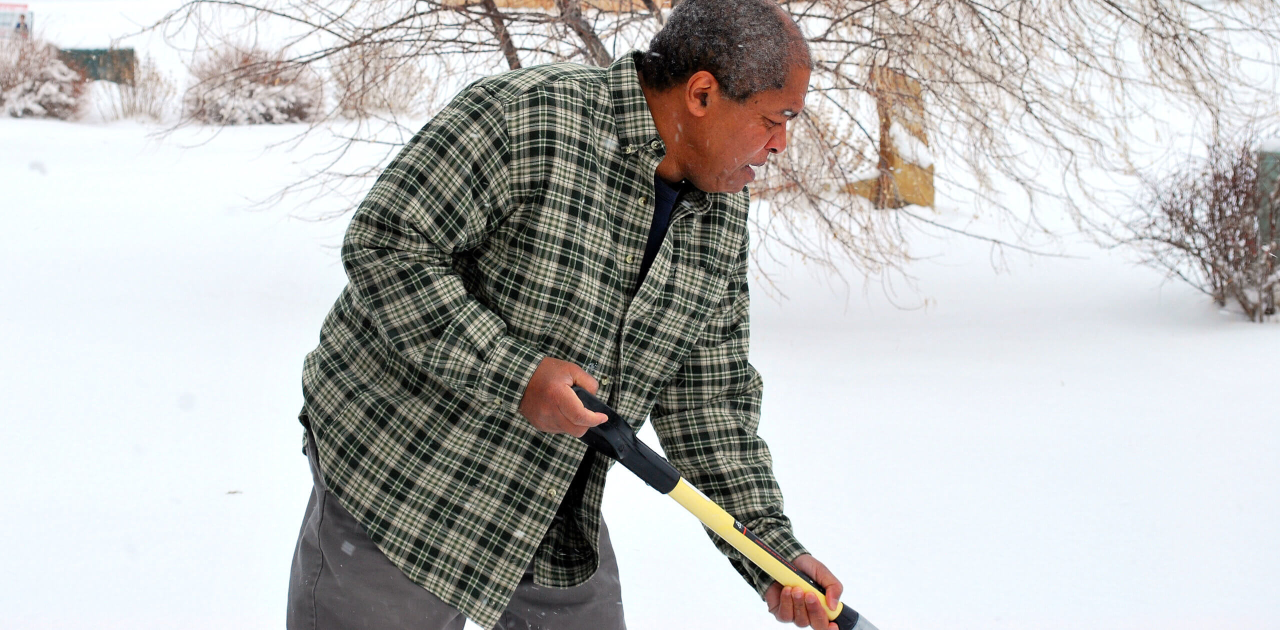 Black man in a plaid shirt clears his driveway after a snowstorm.
