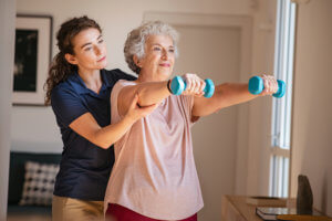 A young physical therapist assists an older female patient with exercises using hand weights.