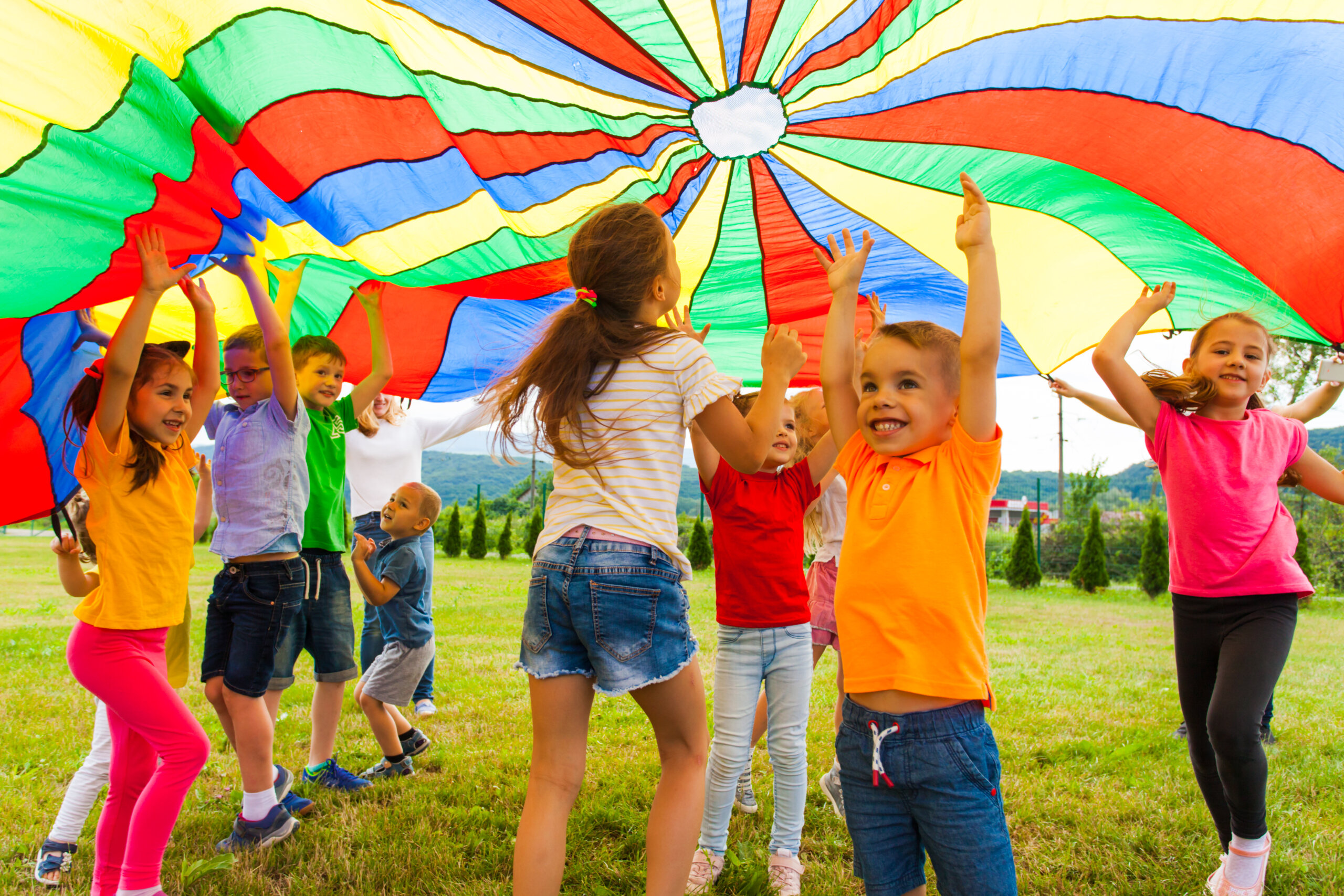 A group of children play outside under a colorful parachute.