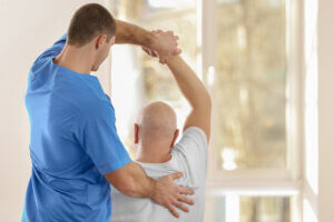 Physical therapist helping older man stretch his shoulder.